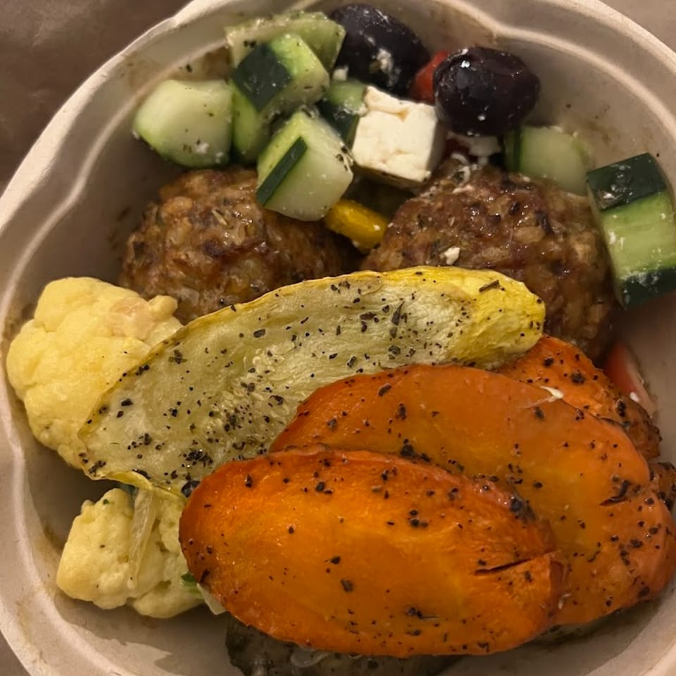 A healthy Green Symphony bowl with meatballs, roasted vegetables, cucumbers, olives, and feta cheese.