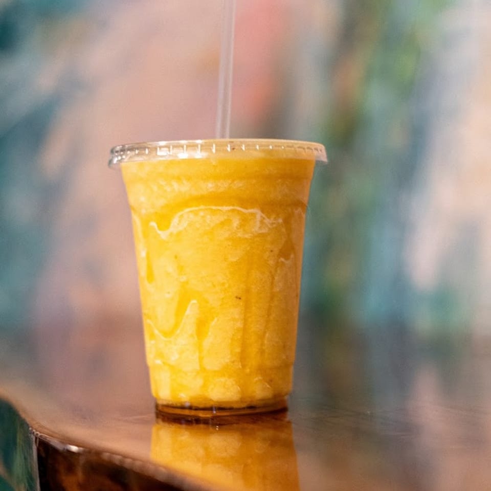 A vibrant yellow Green Symphony smoothie in a clear cup with a straw, on a reflective surface.