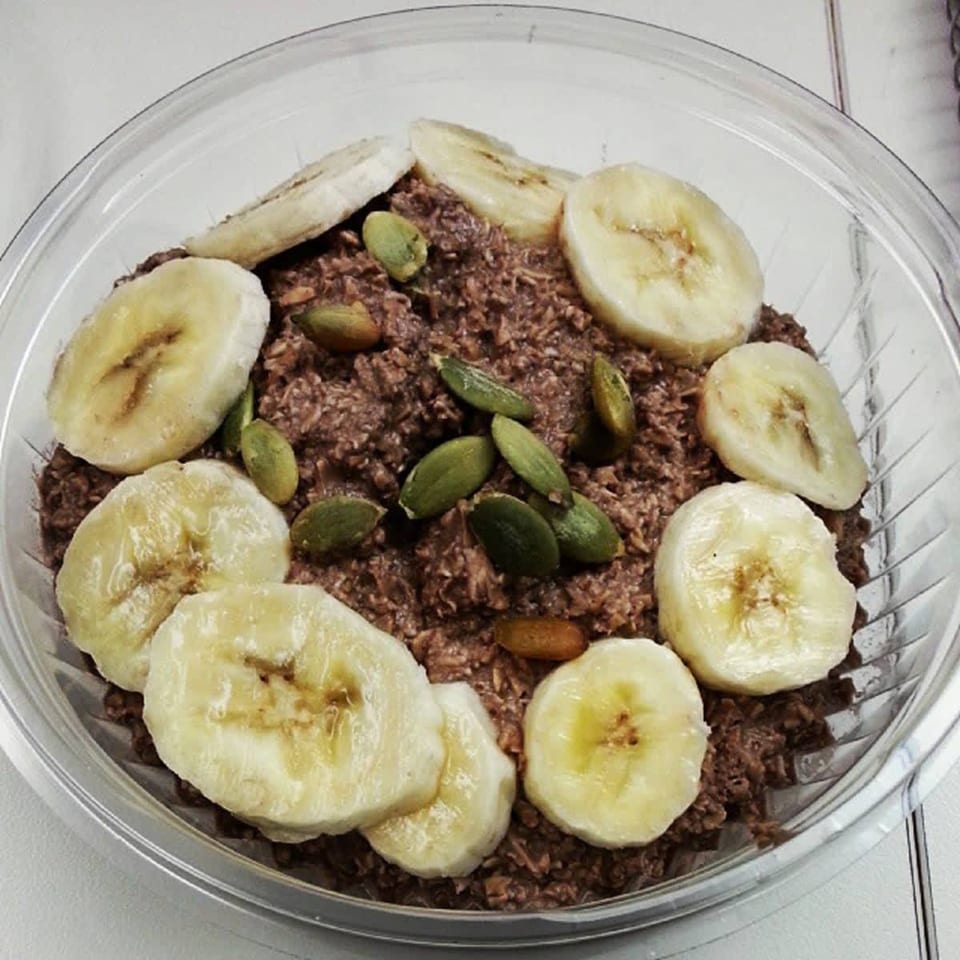 Green Symphony's healthy chocolate oatmeal topped with banana slices and pumpkin seeds in a clear bowl.
