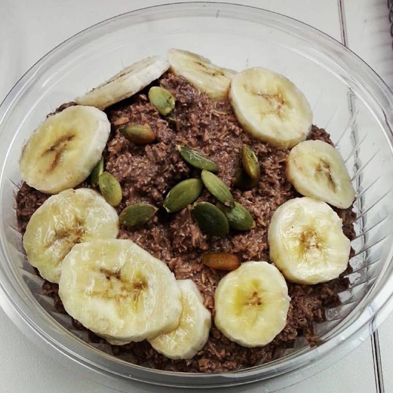 Green Symphony's healthy chocolate oatmeal topped with banana slices and pumpkin seeds in a clear bowl.