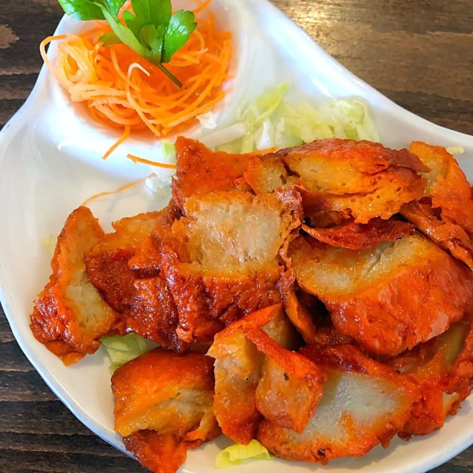 Green Symphony's crispy orange vegan chicken with shredded carrots and lettuce on a white plate.